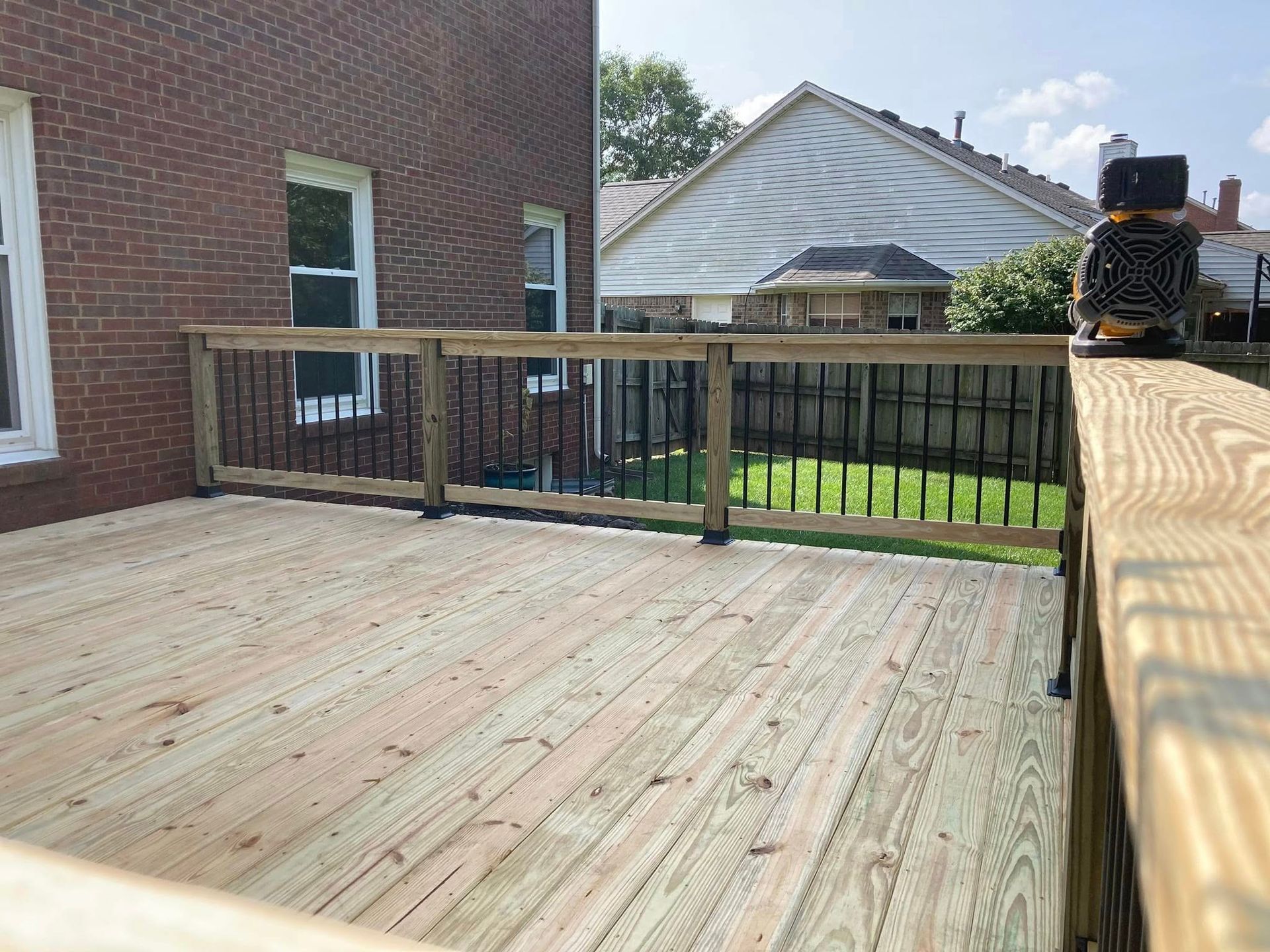 Wooden deck beside a brick house, with black railing and a backyard view.
