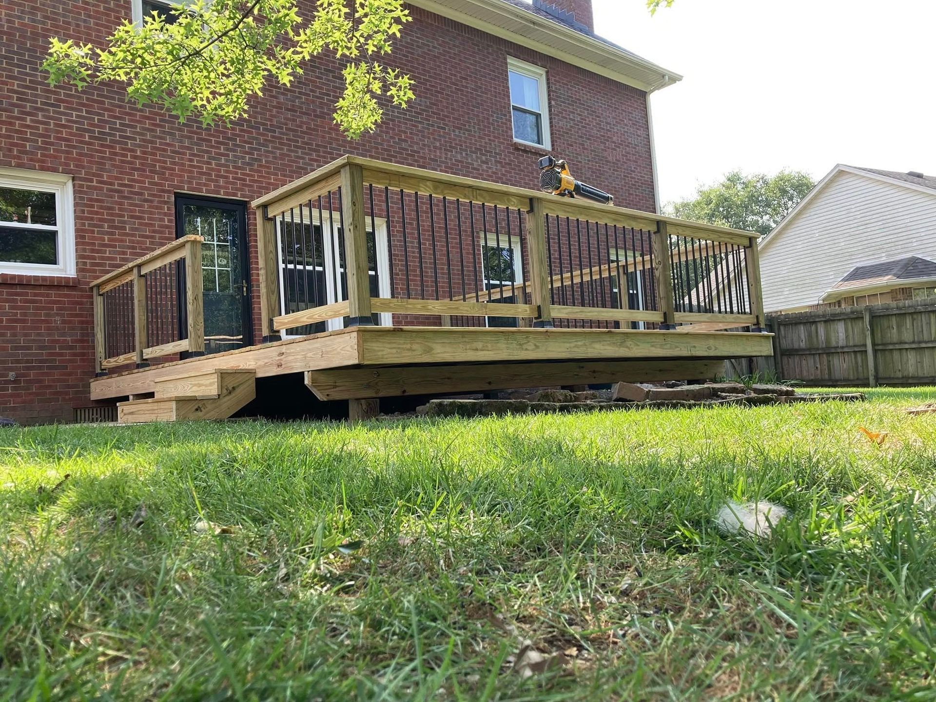 Backyard wooden deck attached to a brick house, with steps and a grassy yard.