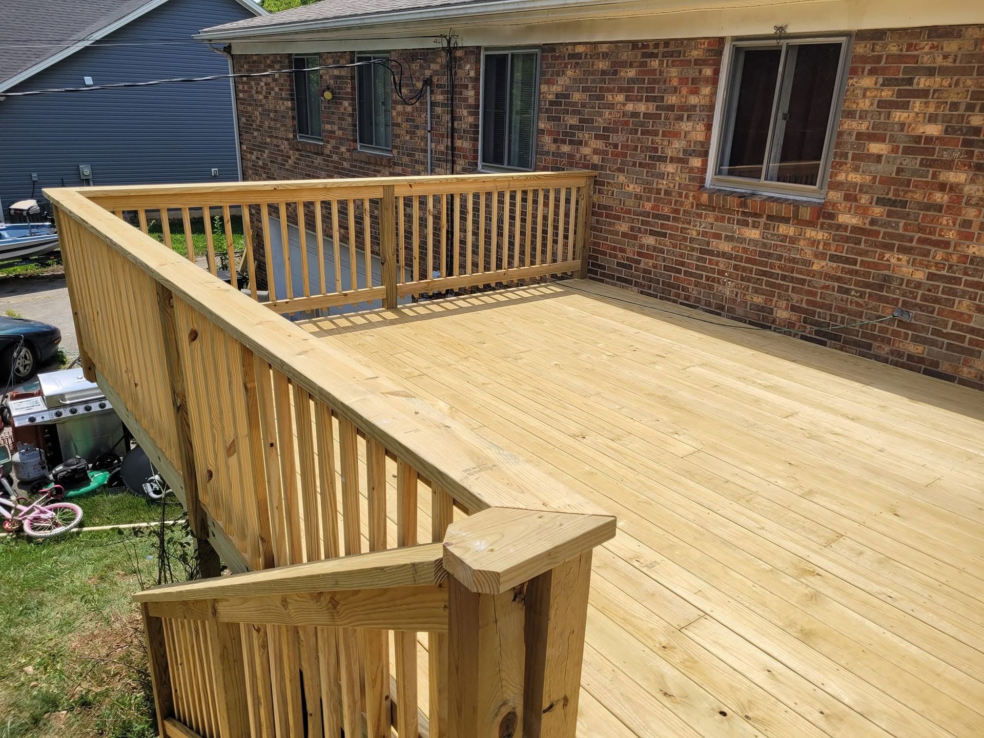 Wooden deck under construction beside a brick house, with railing and stairs