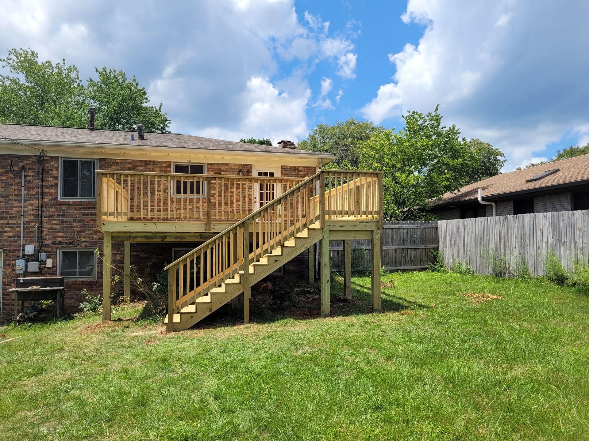 Wooden backyard deck with stairs attached to a brick house, under a partly cloudy sky.