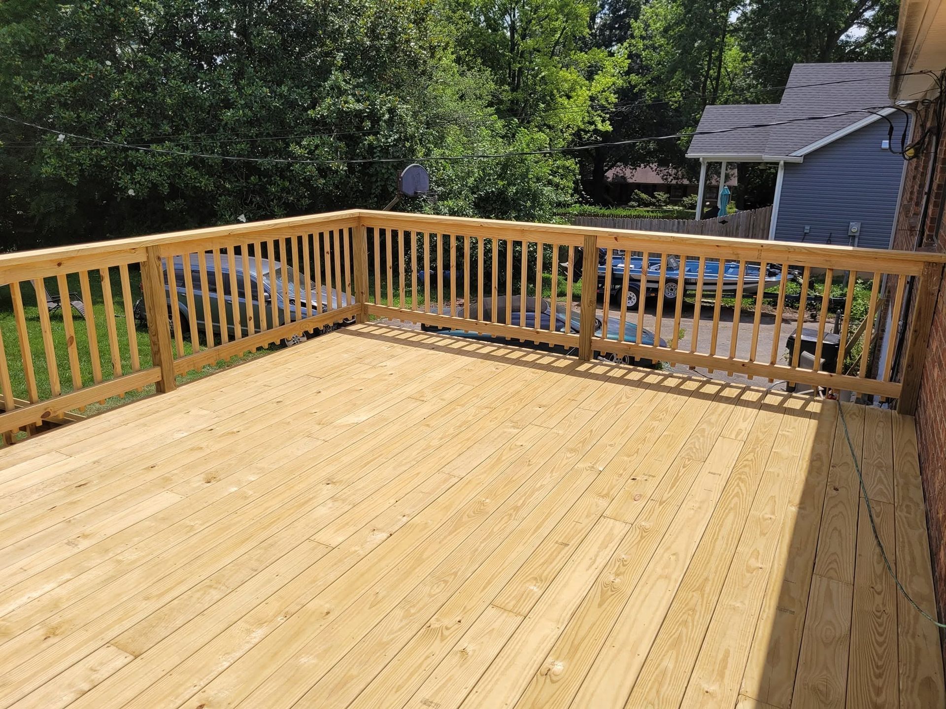 Wooden deck with railing overlooking a backyard and house, in daylight