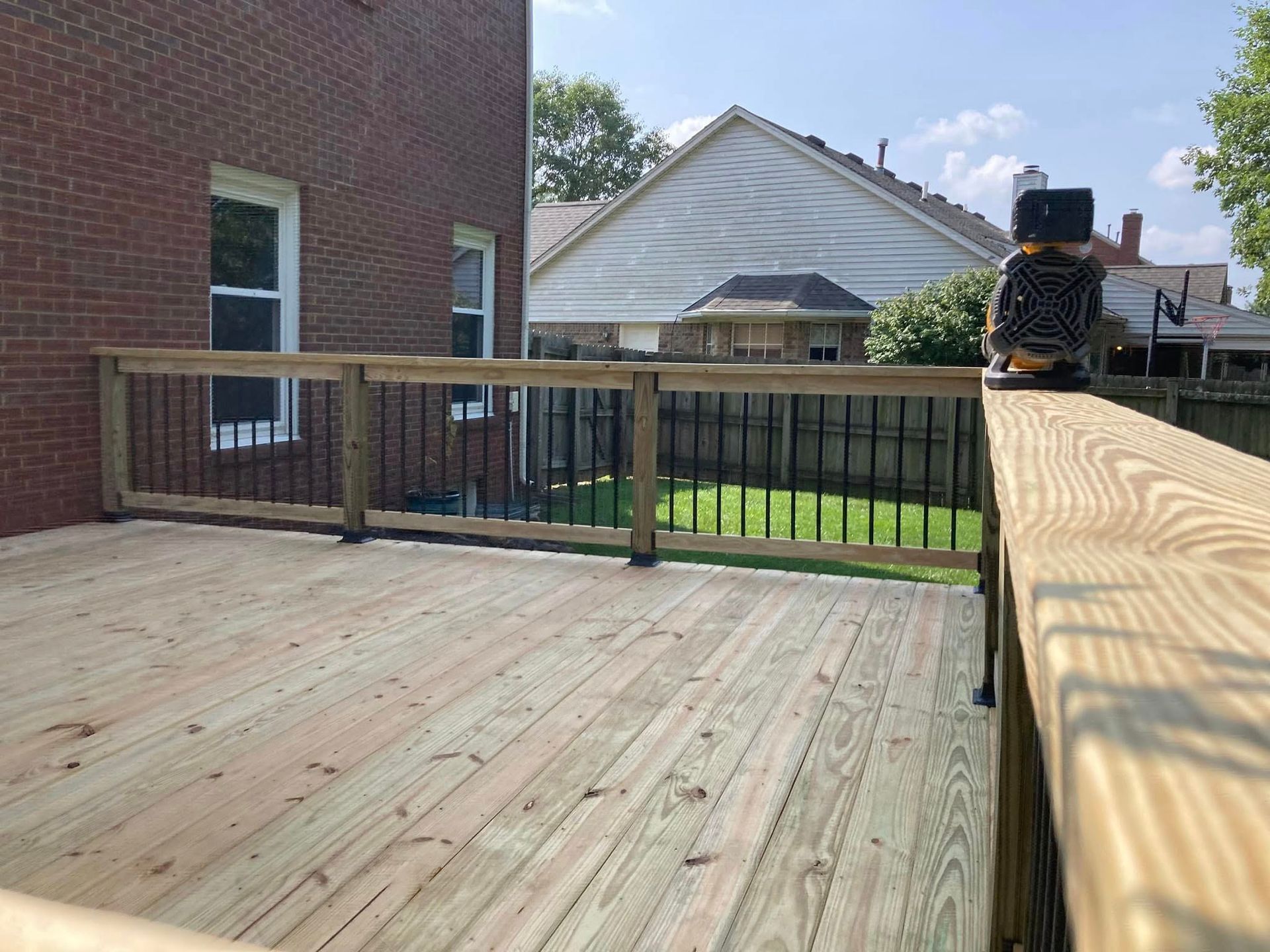 Wooden deck with railing overlooking a backyard and neighboring houses on a sunny day