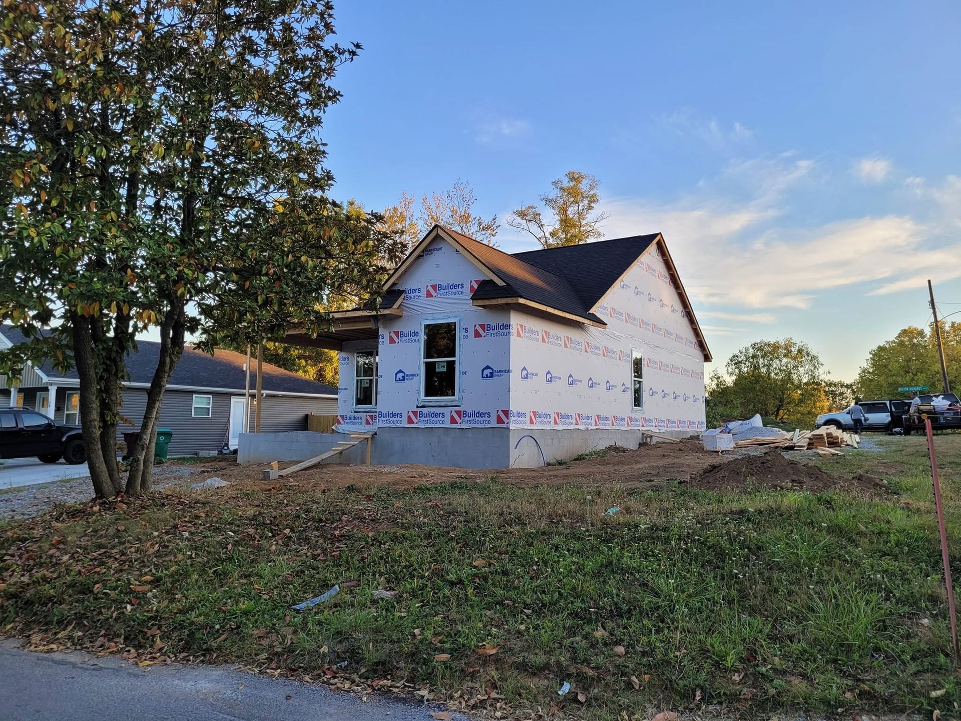 Partially built white house with dark roof on a grassy lot at sunset