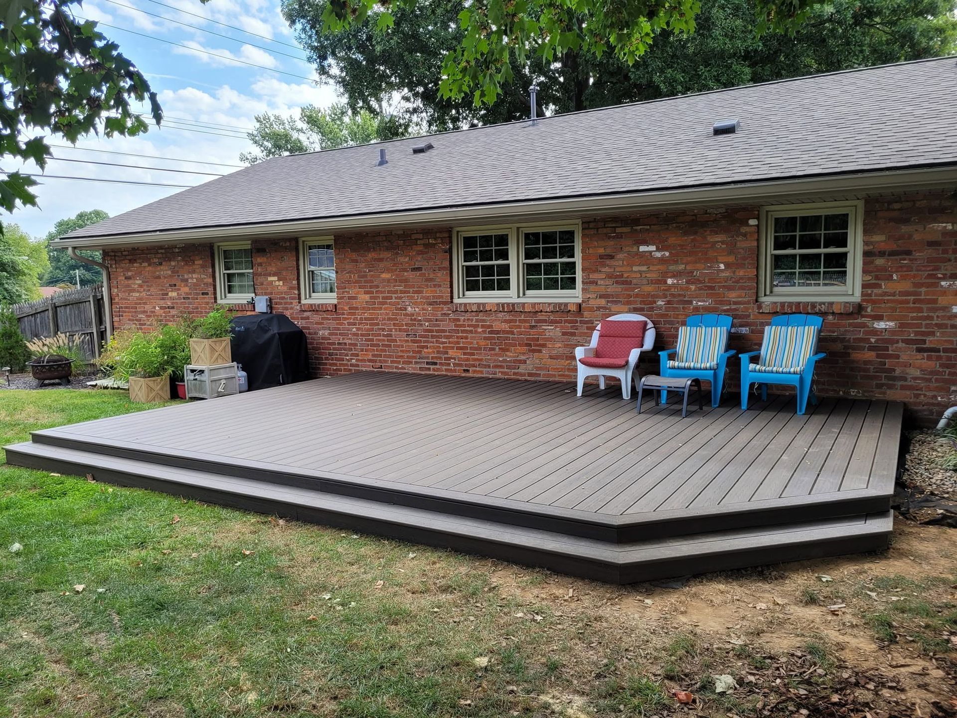 Back deck beside a brick house with patio chairs and grill in a grassy yard