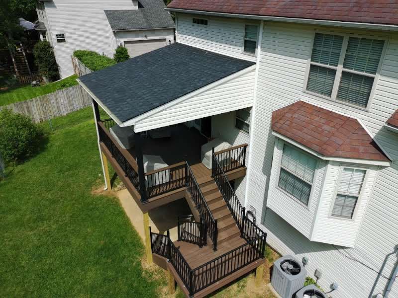 Backyard deck with black railings, stairs, and a covered patio attached to a white house
