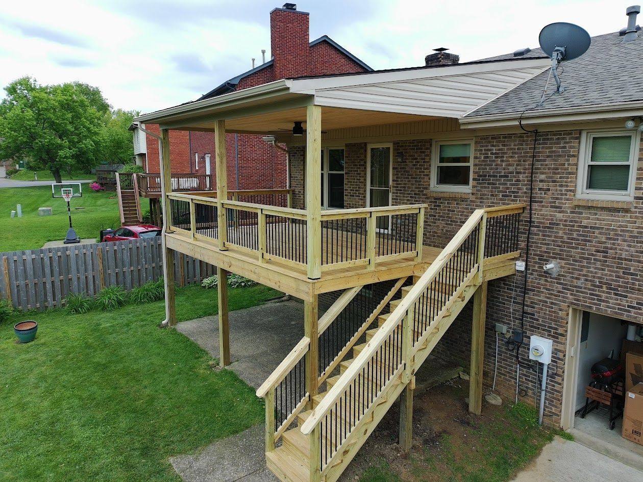 Wooden backyard deck with stairs attached to a brick house, overlooking a grassy yard.
