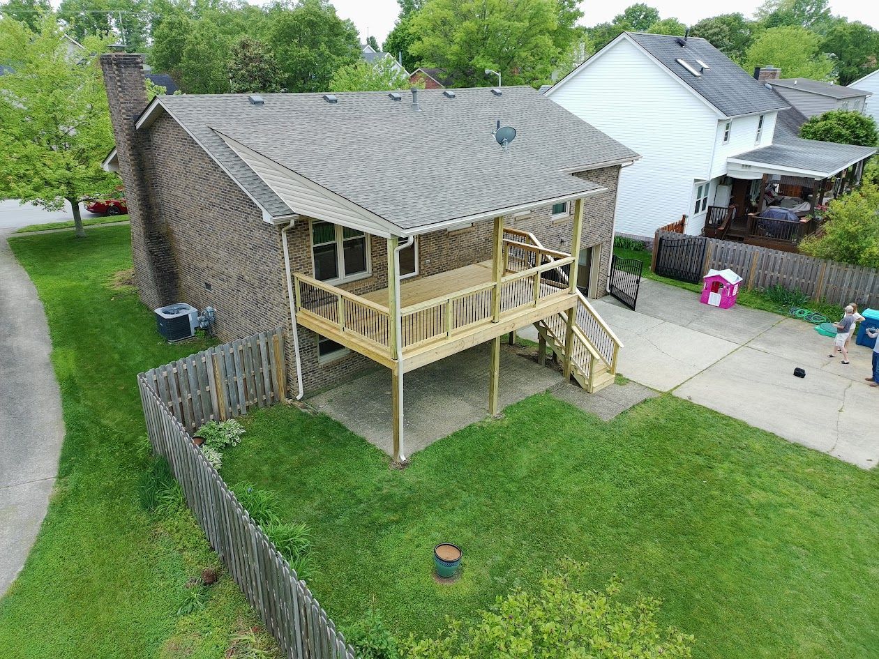 Backyard with a raised wooden deck attached to a brick house, fenced lawn, and driveway beside neighboring homes