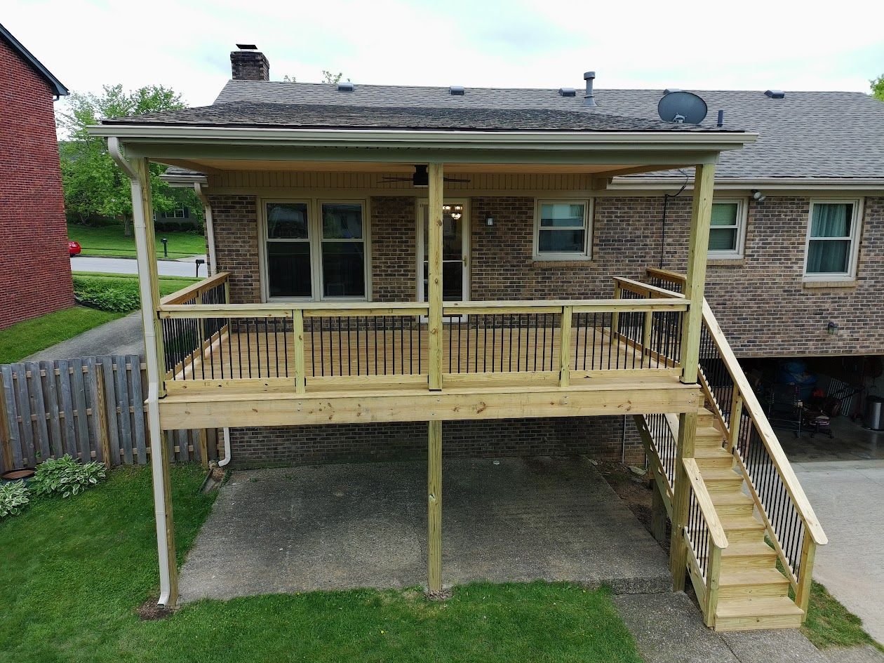 Raised wooden deck with railings and stairs attached to a brick house in a suburban yard