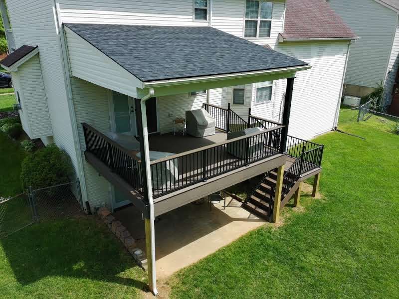Backyard house with a small covered porch, black railings, and stairs leading to a grassy yard