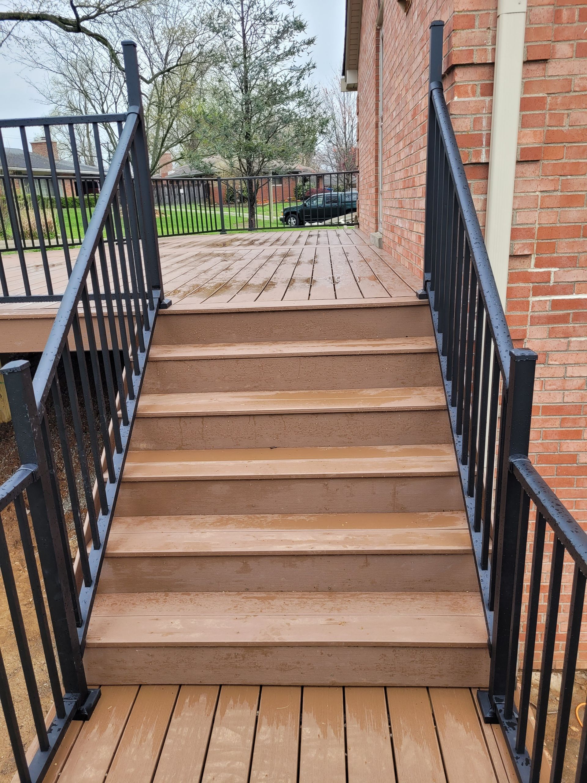 Wooden staircase with black railings leading to a brick porch and walkway outdoors