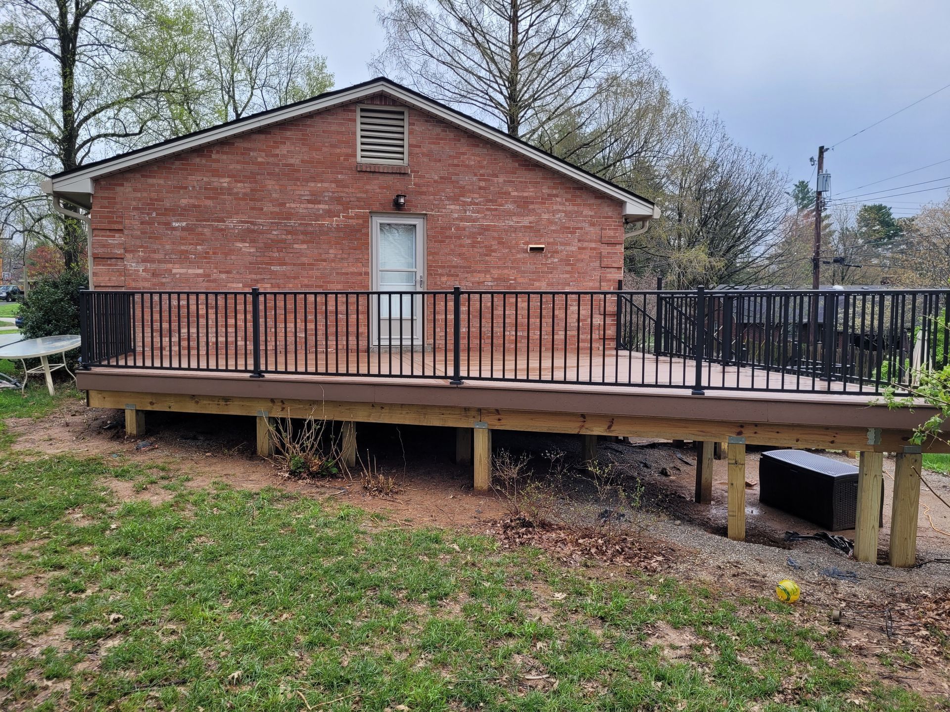 Brick building with a raised wooden deck and black railing in a grassy yard