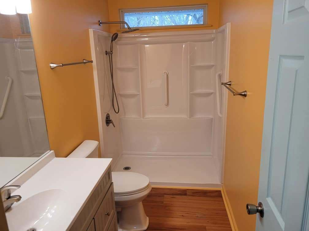 Compact bathroom with white vanity, toilet, tub-shower combo, and wood floor.