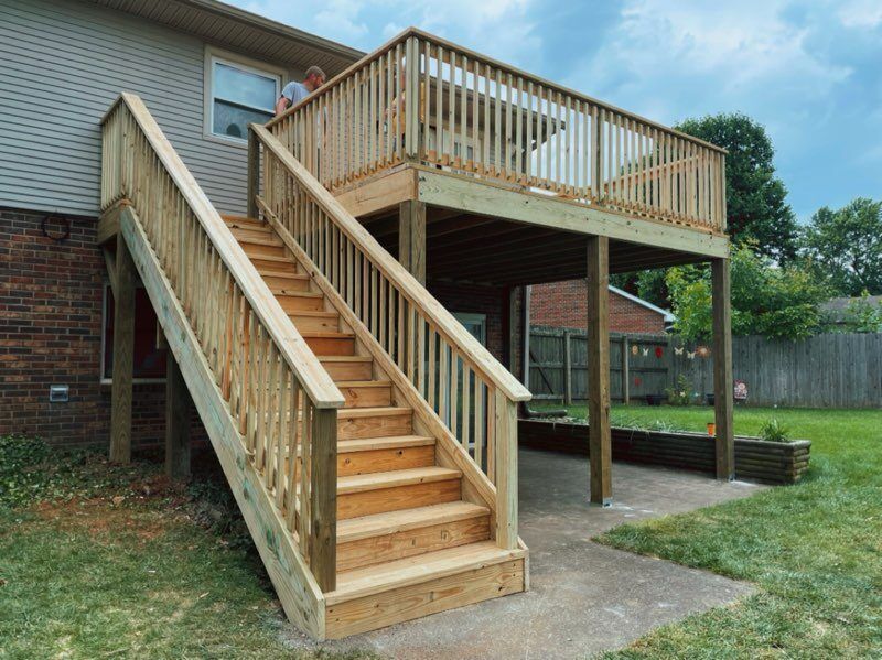 Wooden deck and staircase with railings attached to a brick house in a backyard.