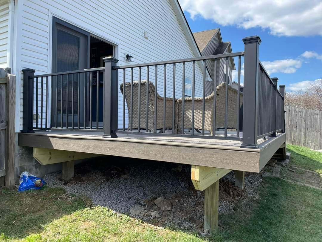 Raised backyard deck with black railings beside a white house, holding outdoor furniture and a grill cover.