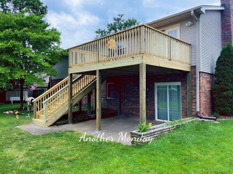 Back deck with stairs and railing over a covered patio on a brick-and-siding house, with green lawn and trees