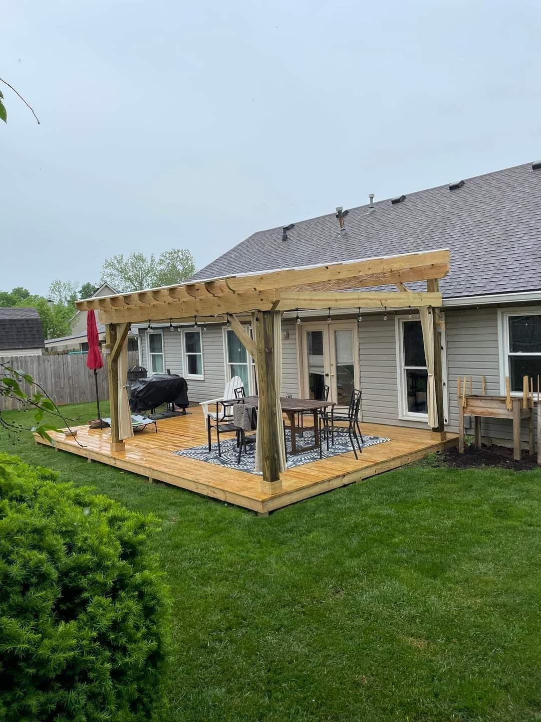 Backyard patio with wooden pergola framing outdoor seating beside a house