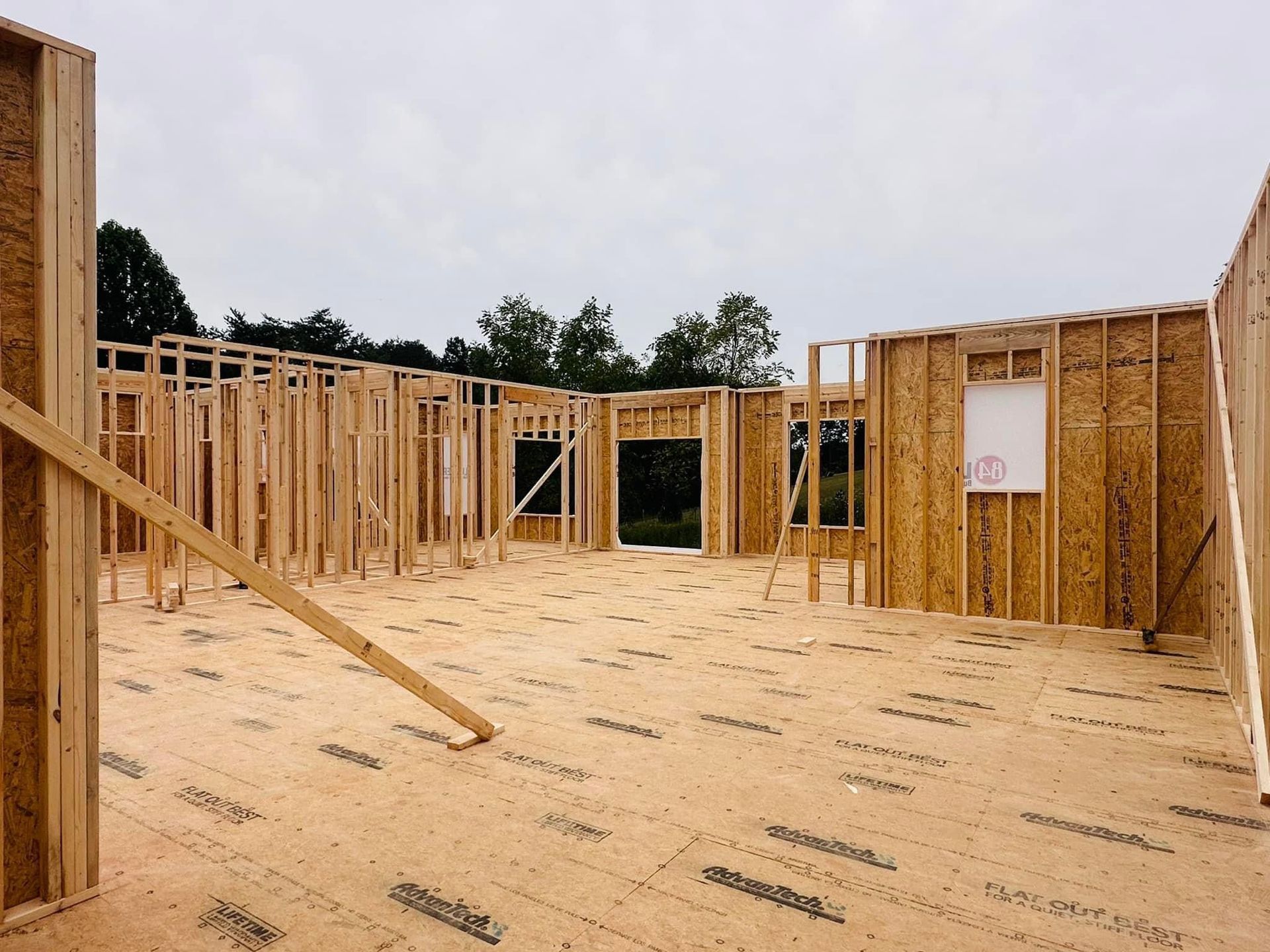 Wood-framed house under construction with plywood subfloor and open framing under a cloudy sky