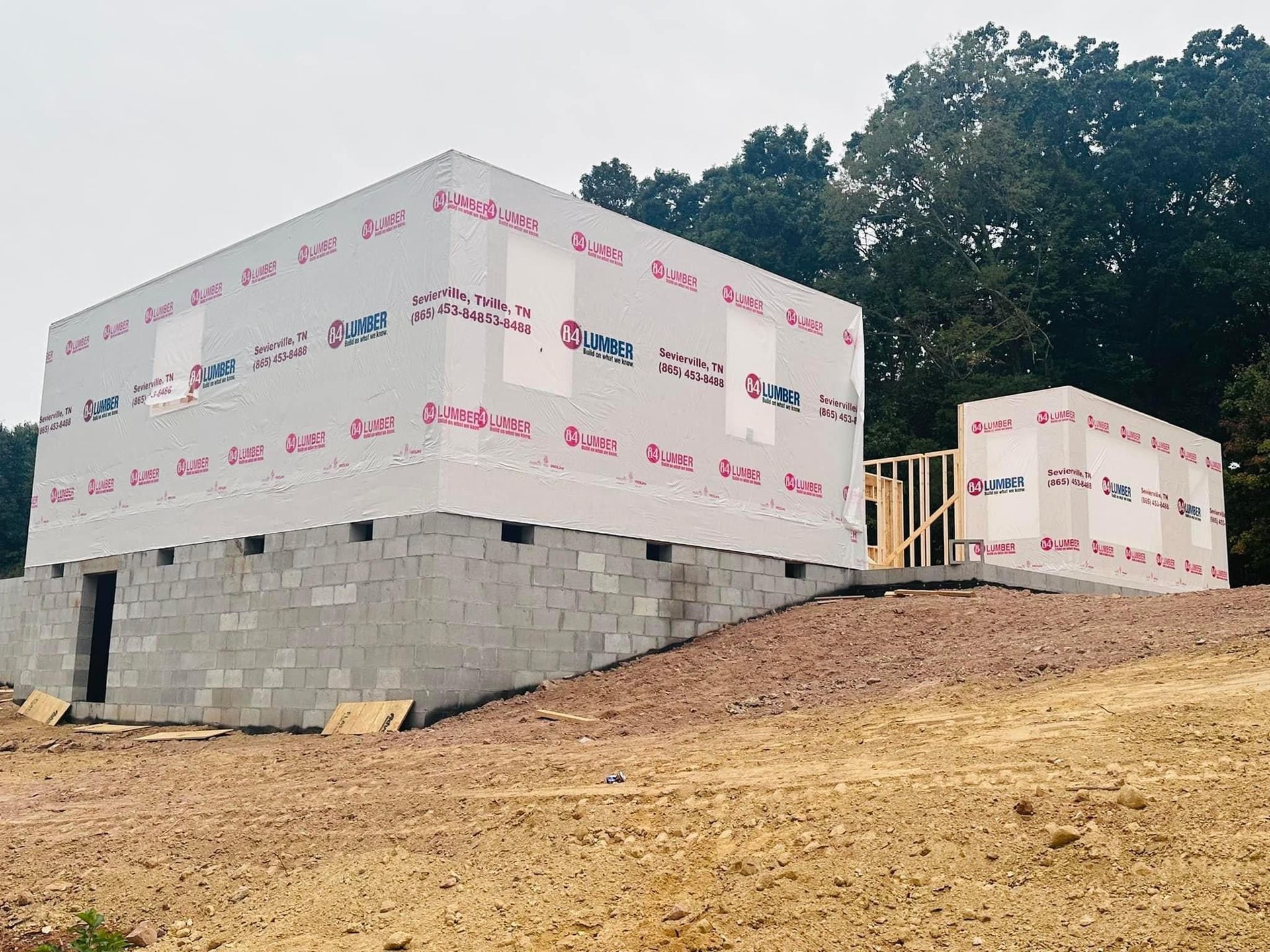 Two white-clad buildings under construction on a sloped dirt and cinder block foundation.