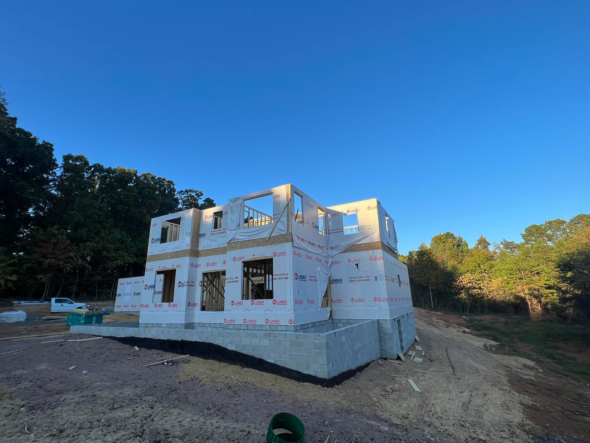 Partially built white house with exposed framing on a dirt lot under a clear blue sky
