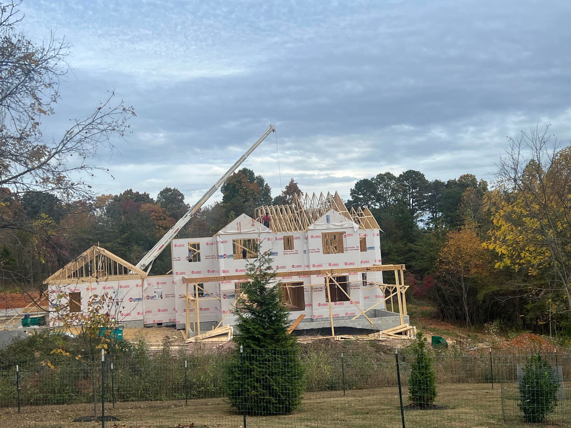 Partially built house under construction with crane, framed walls, and autumn trees in the background