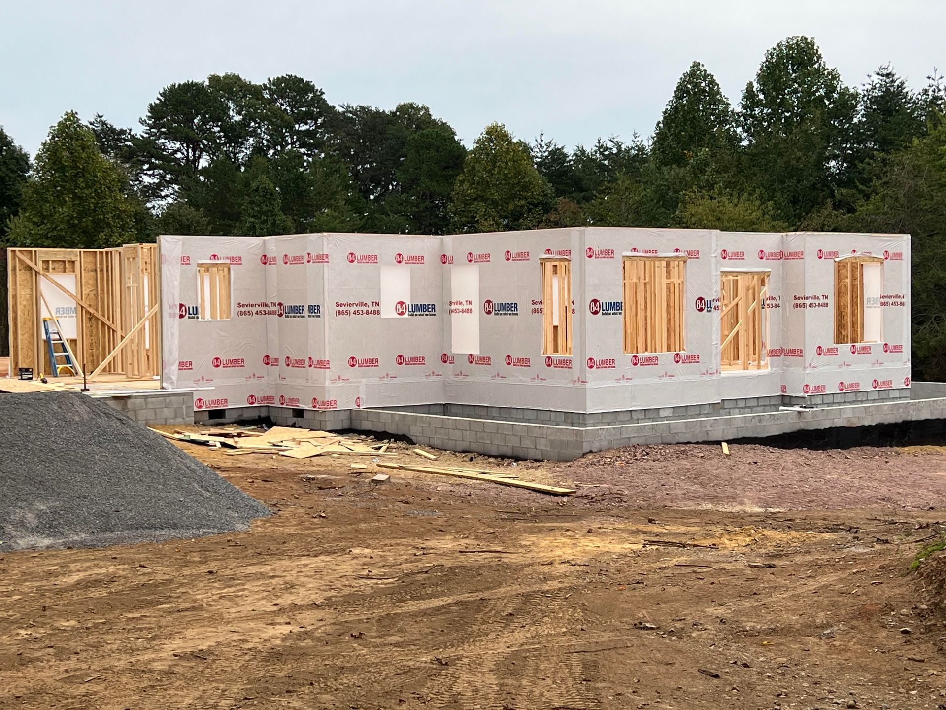 House under construction with exposed wooden framing and wrapped exterior walls on a dirt lot