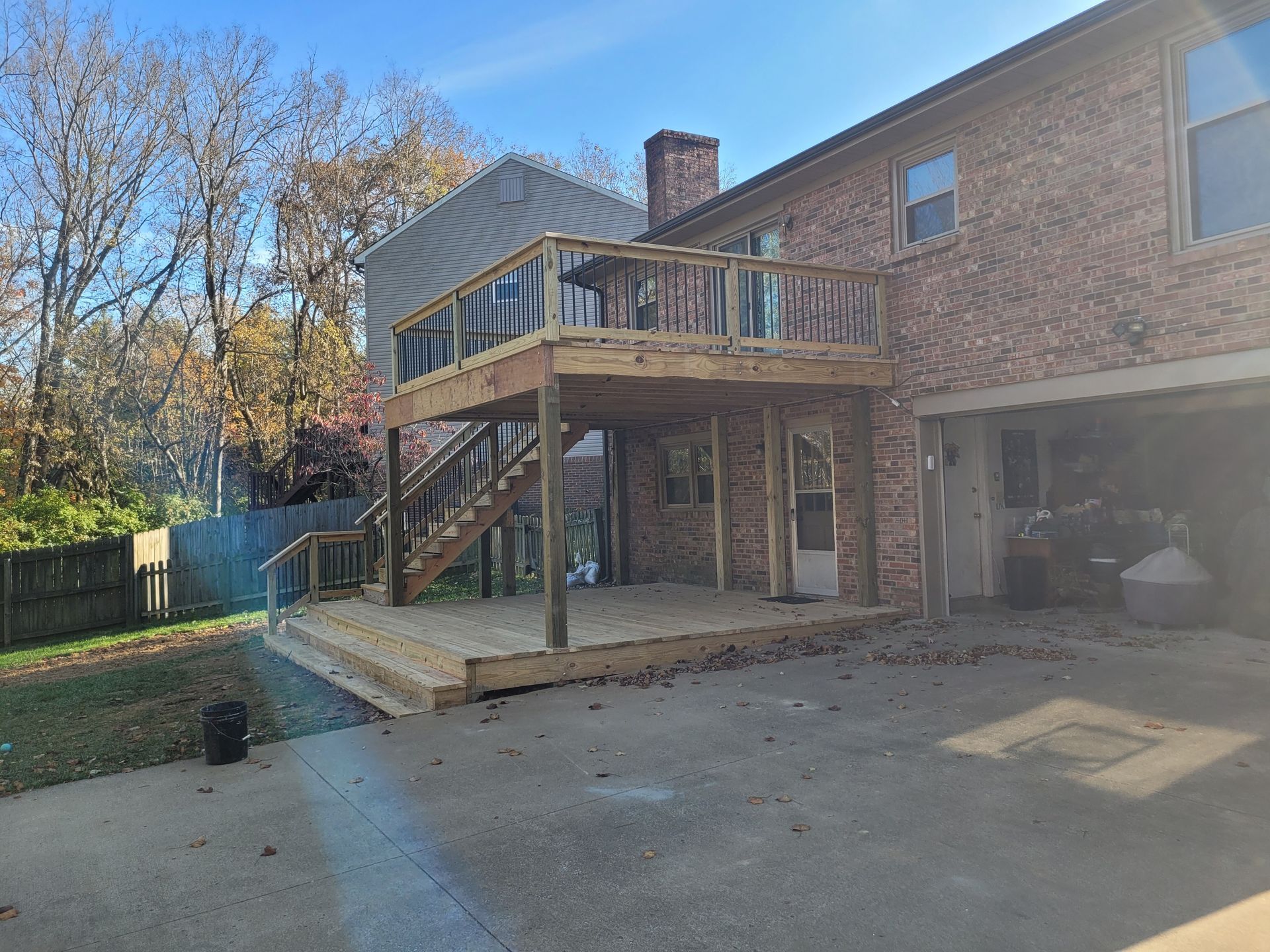 Brick house with elevated wooden deck and stairs above a concrete patio in a sunny backyard