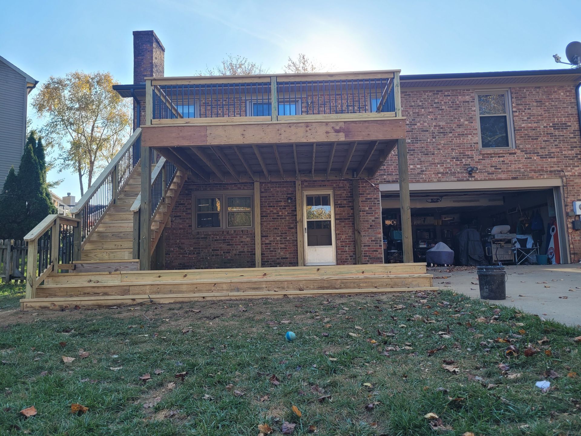 Brick house with a raised wooden deck and stairs overlooking a grassy yard, with an open garage on the right.