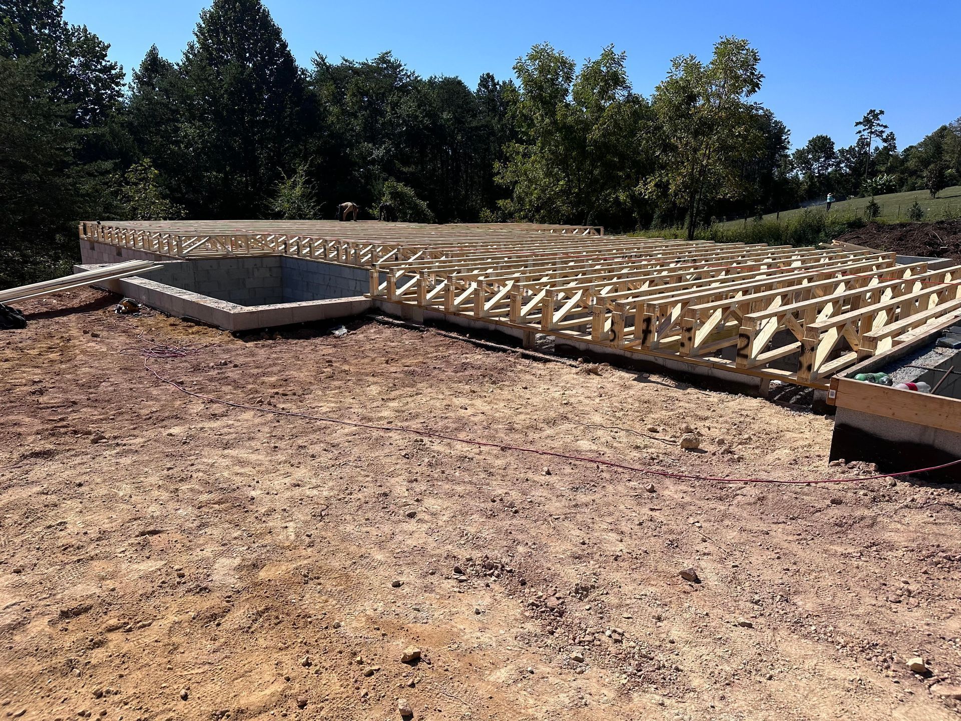 Wooden foundation framing on bare ground at a construction site, with trees in the background
