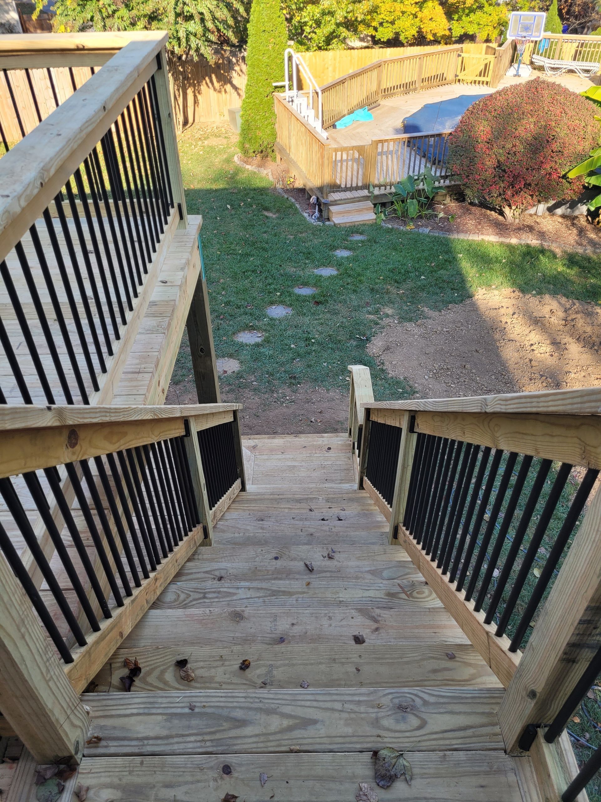 Wooden backyard stairs with black railings leading down to a grassy yard and deck area