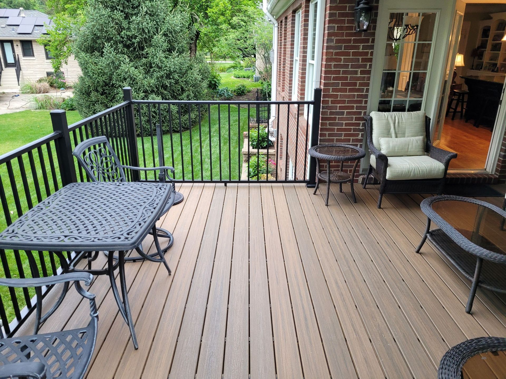Wooden deck with black railing, patio furniture, and open sliding door overlooking a green yard
