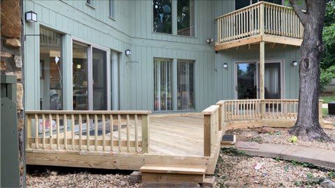 Wooden deck and railing outside a beige house with sliding doors and a tree in the yard