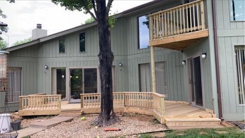 Two-story green apartment building with wood decks and a large tree in front