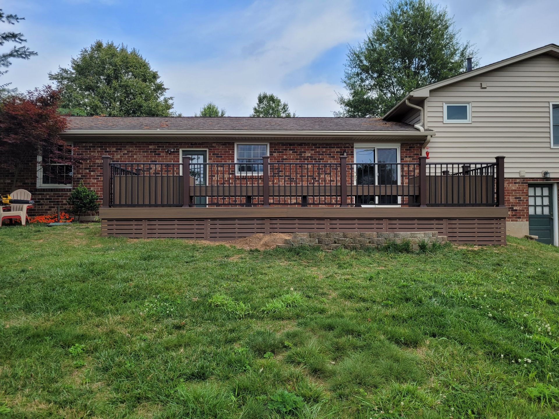Backyard deck with brown railing, brick house, and grassy lawn under a blue sky