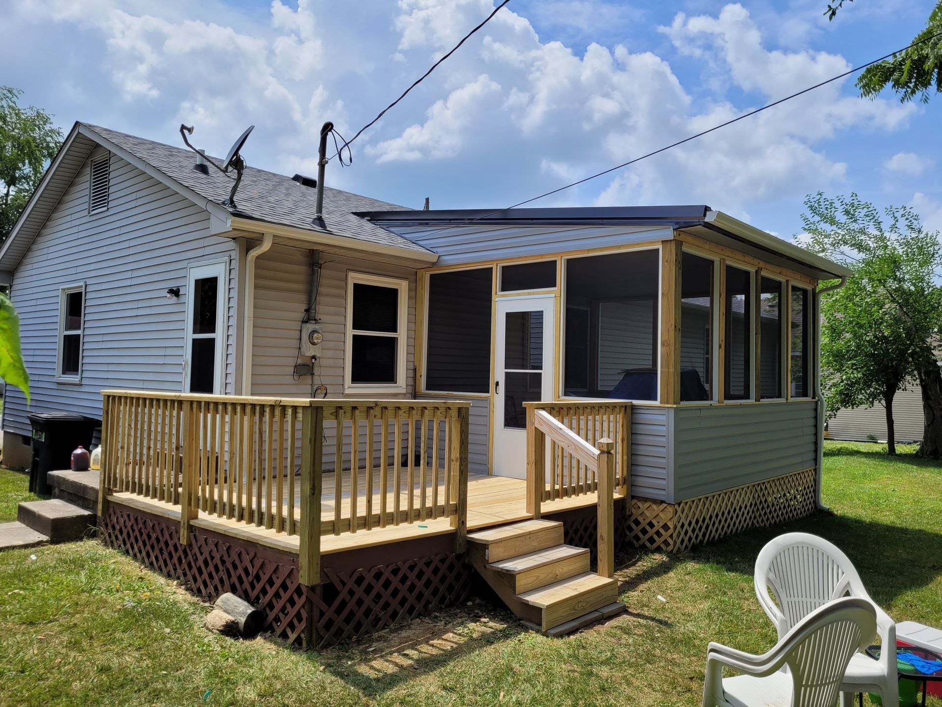 Small white house with a wooden front porch, steps, screened side enclosure, and a white chair on the lawn