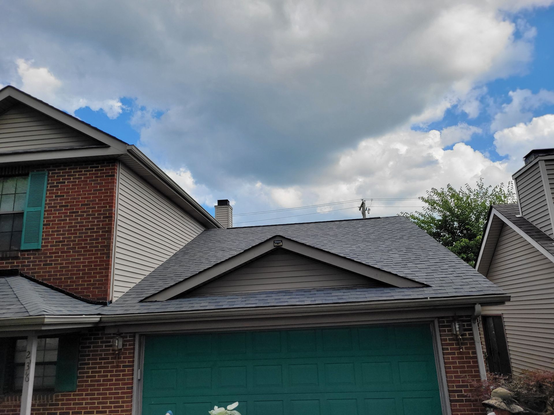 Suburban house with green garage door and gray roof under a cloudy sky