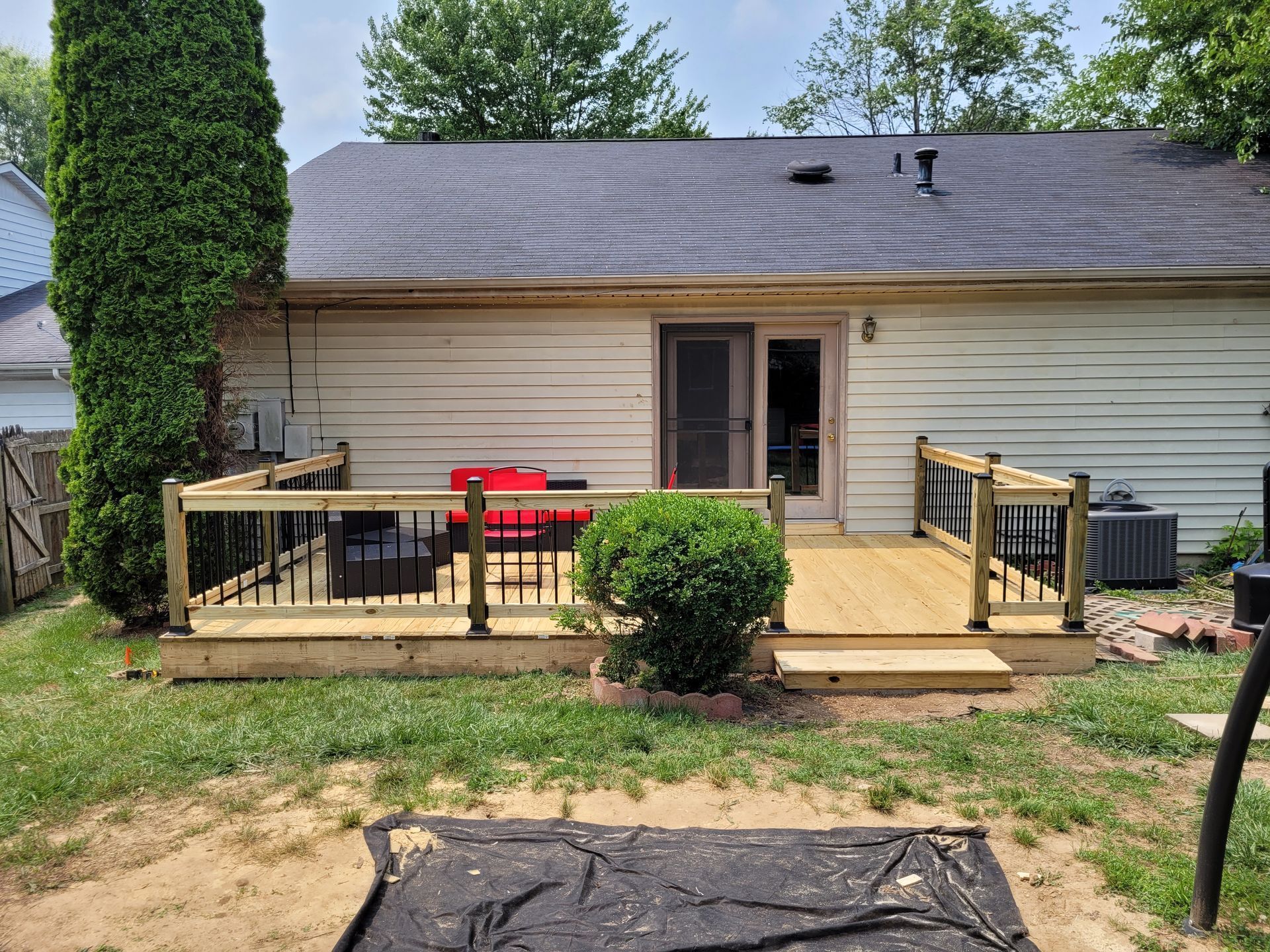Backyard deck with wooden railings, red chairs, and a house wall with a door and window