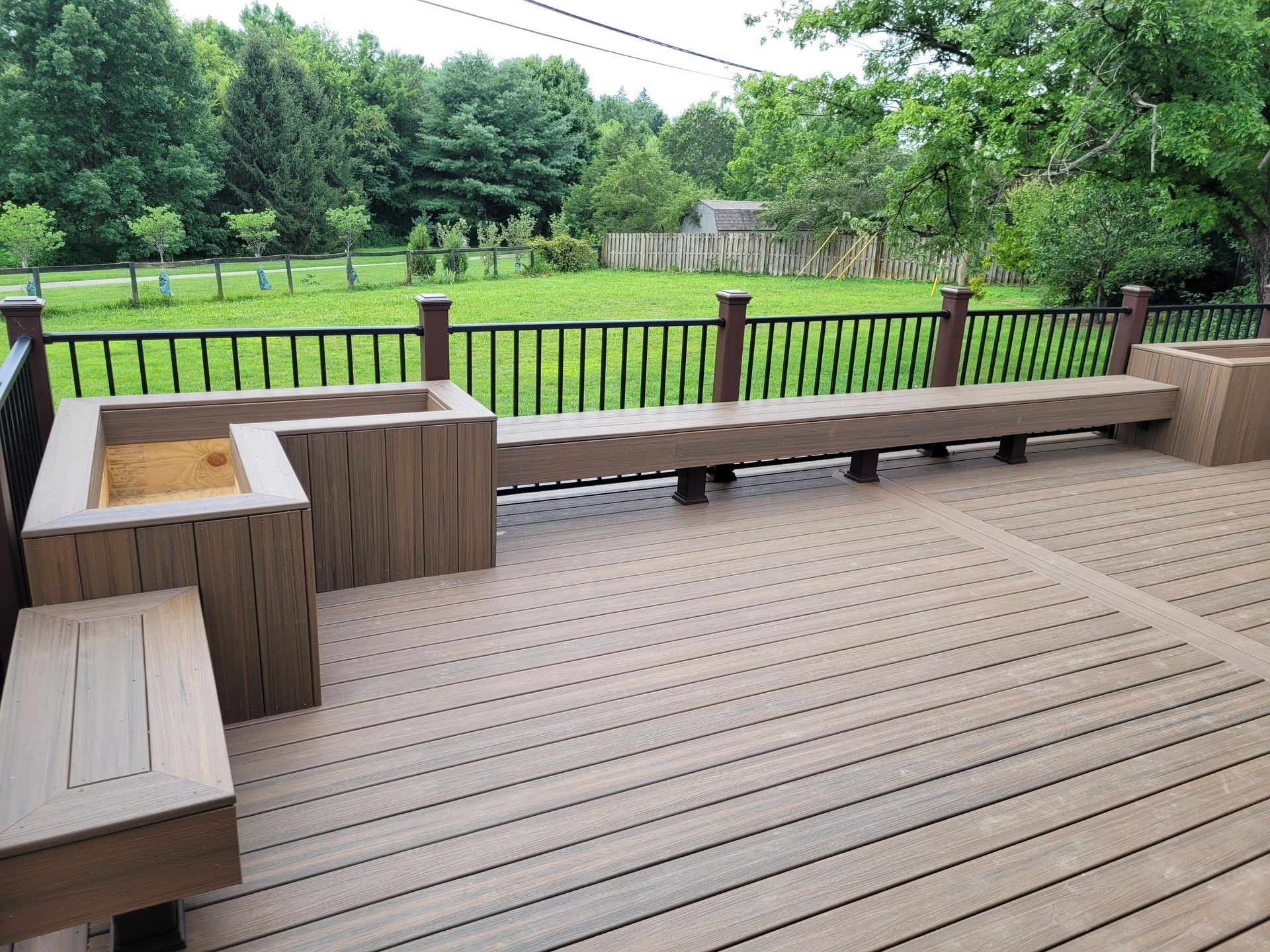 Wooden deck with built-in seating overlooking a green backyard and fence
