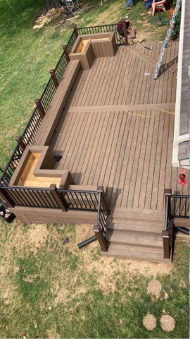 Wooden backyard deck with railings, steps, and built-in benches beside a grassy yard.