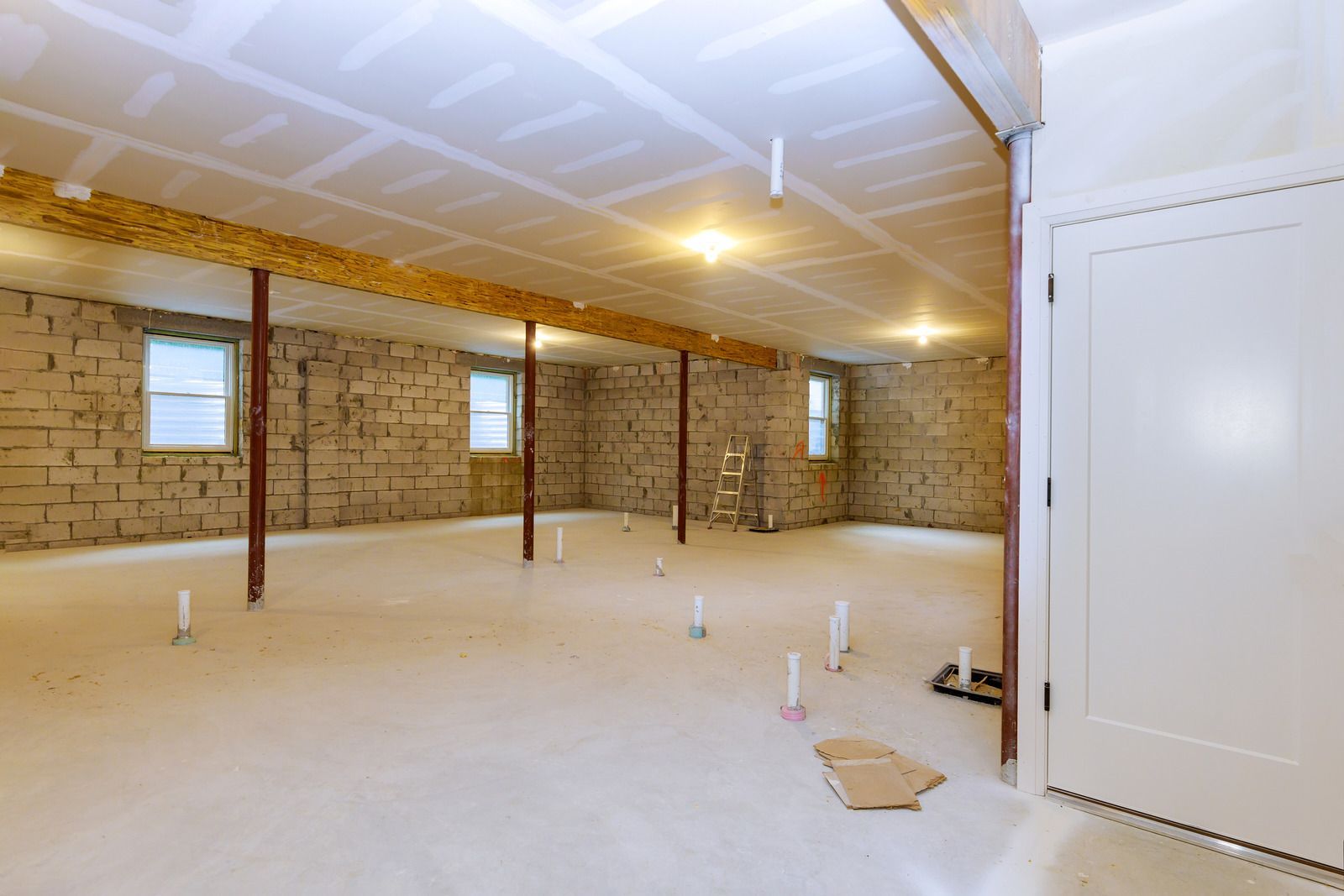 Empty unfinished basement with exposed brick walls, white ceiling, concrete floor, and utility pipes.