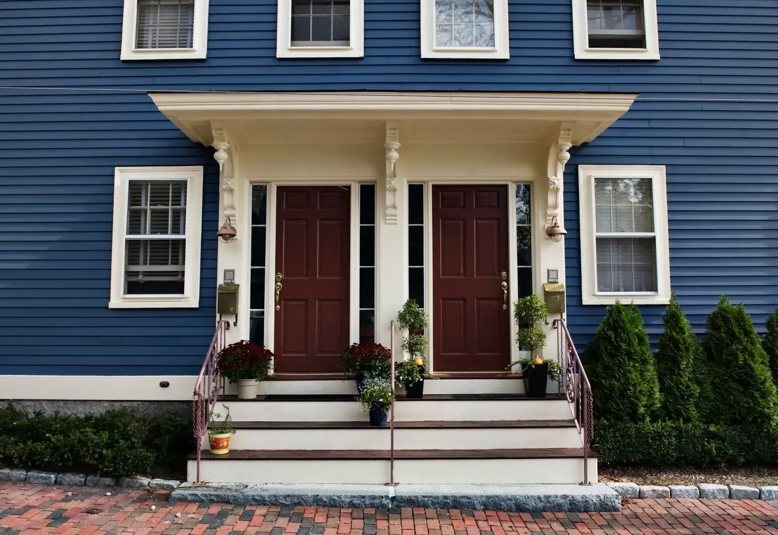 Blue house front with two maroon doors, white trim, and steps leading to a brick walkway