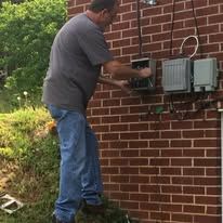 A man is working on an electrical box on the side of a brick building.