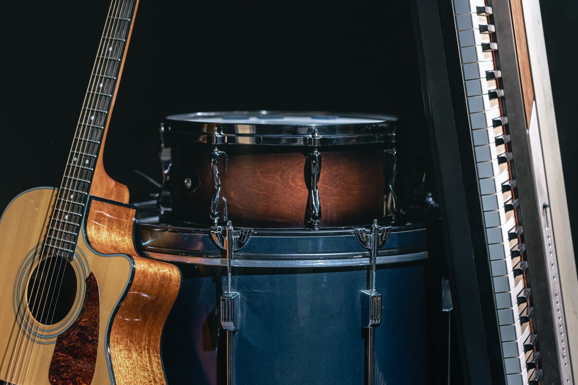 Acoustic guitar, snare drum, and keyboard in a dark studio setting.