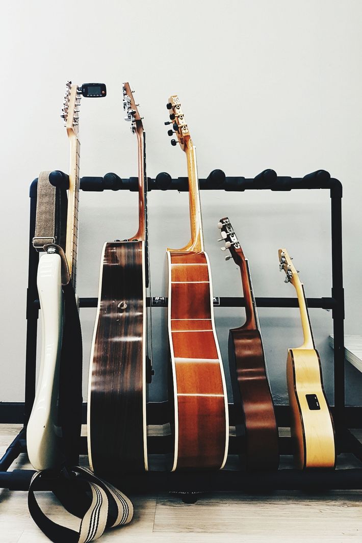 Guitars on a black stand against a gray wall. Several acoustic and electric guitars of various sizes.