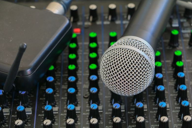 Microphone and wireless receiver on a sound mixing board with multiple knobs and sliders.