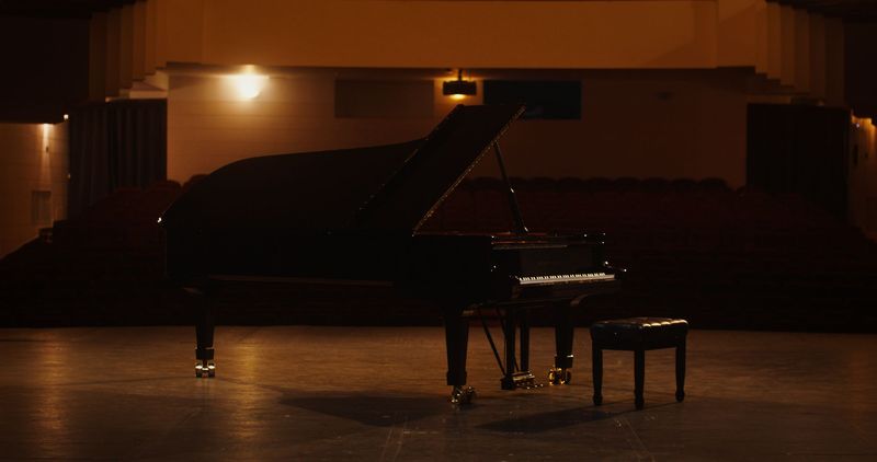 Grand piano on a stage, lit by warm light, in a dark auditorium.