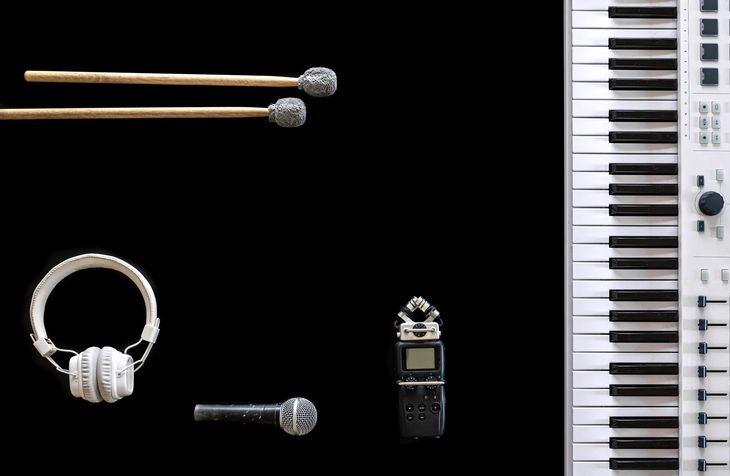 Percussion mallets, headphones, microphone, recorder, and keyboard on black background.