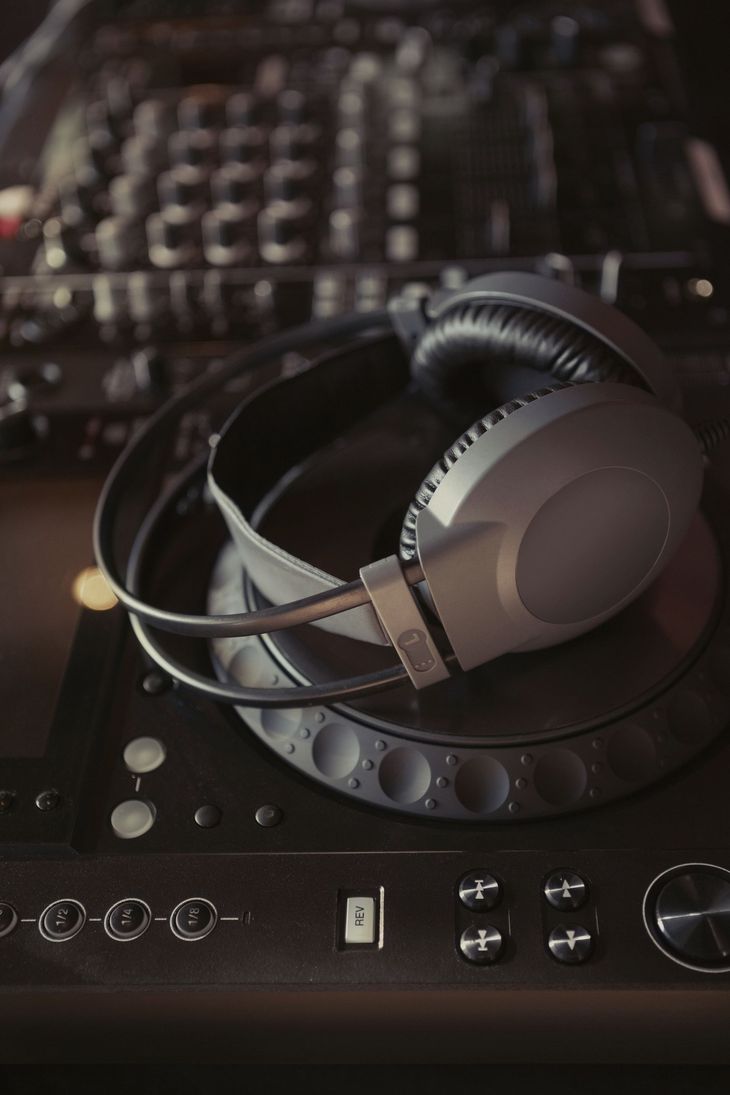 Headphones rest on a DJ turntable, positioned in front of a mixing board; dim lighting.