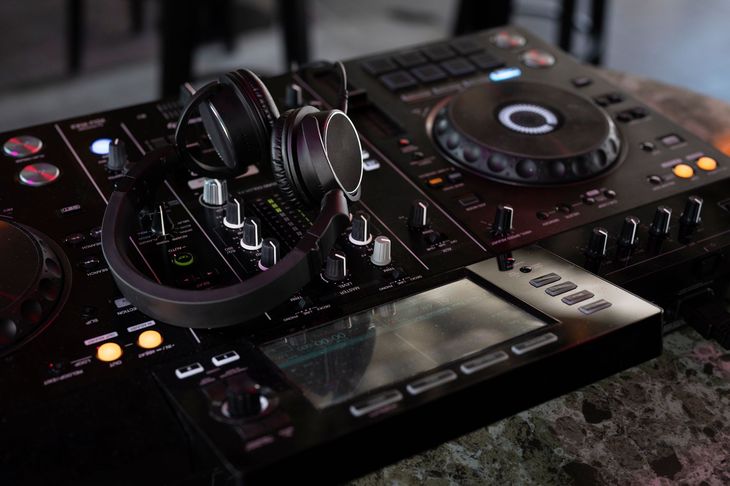 DJ setup with headphones, black mixer, and turntables on a table in a dimly lit room.