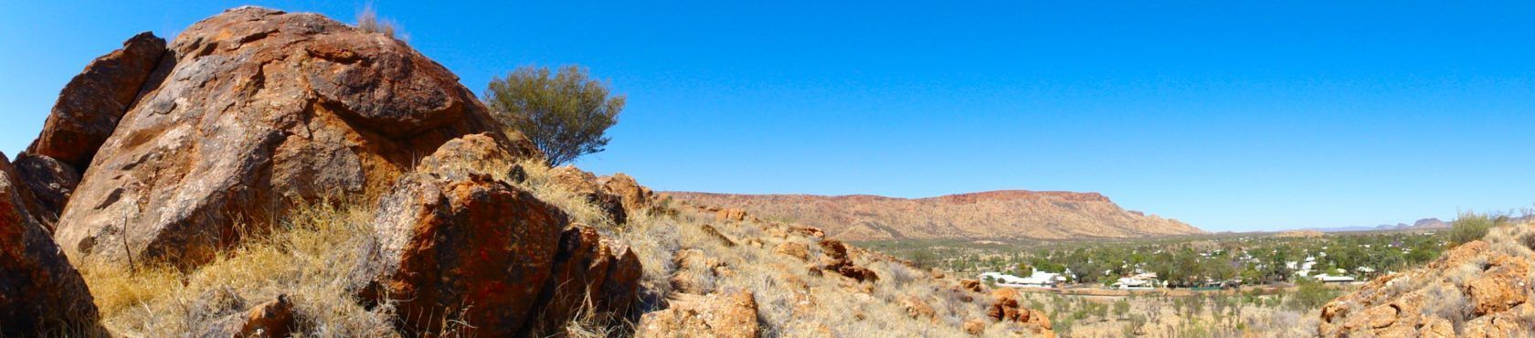 Panoramic view of a rocky landscape under a clear blue sky. Small trees are visible in the distance.