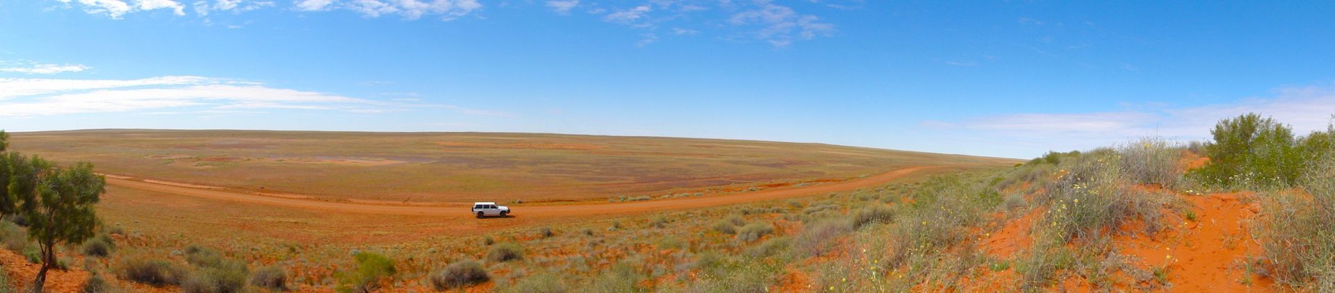 Panoramic view of a desert landscape with a vehicle in the distance under a blue sky.